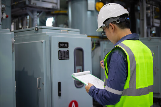 Gas insulated switchgear substation engineer inspects equipment carefully wearing safety helmet and reflective vest in industrial power facility ensuring operational safety and reliability