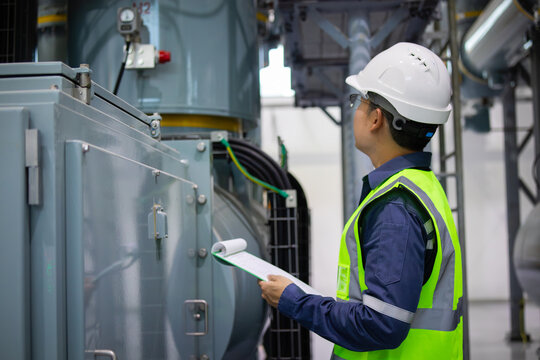 Gas insulated switchgear substation engineer inspects equipment carefully wearing safety helmet and reflective vest in industrial facility ensuring operational safety and reliability