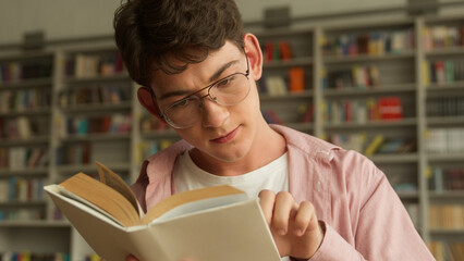 Close up concentrated Caucasian male student man guy teenager reading book poem story textbook...