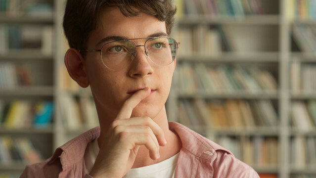 Close up Caucasian male student man guy teenager thinking pensive think idea ponder unsure hesitate in library choosing books decide education studying learning in school college research analyze