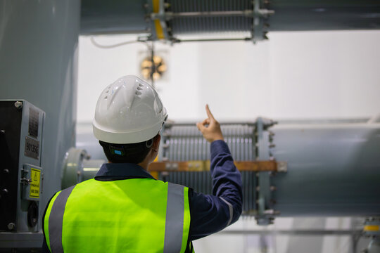 Substation engineer inspects gas insulated switchgear equipment carefully pointing at components in industrial electrical substation ensuring safety and operational standards