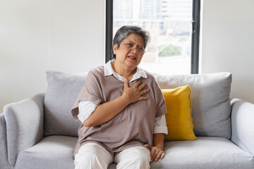 Asian elderly grabbing her chest and feeling pain from heart attack suddenly at home.