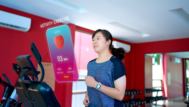 A woman running on a treadmill checks her smartwatch, which projects an augmented reality (AR) display showing real-time fitness data like heart rate, distance, and calories