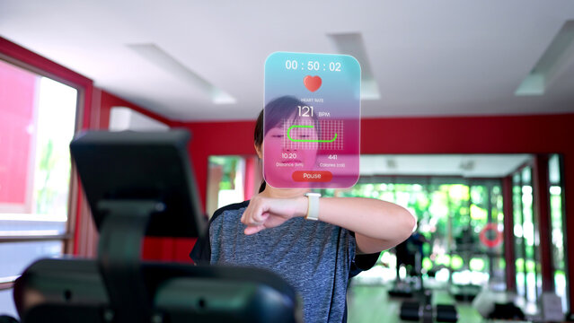 A woman running on a treadmill checks her smartwatch, which projects an augmented reality (AR) display showing real-time fitness data like heart rate, distance, and calories