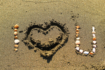 'I love you' written on the sand on the beach with a heart symbol and seashells. Valentine's day concept idea.