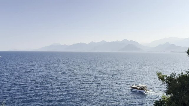 A pleasure boat sails on the sea against the backdrop of a blue open sky and mountains