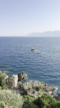 A recreational boat sails on the sea against the backdrop of a blue open sky and mountains (vertical video)