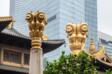 Golden guardian lion statues on columns at Jing'an Temple, Shanghai, contrasted by a modern...