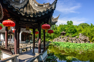 A traditional Chinese garden with winding bridge leading to a pavilion, adorned with red lanterns...