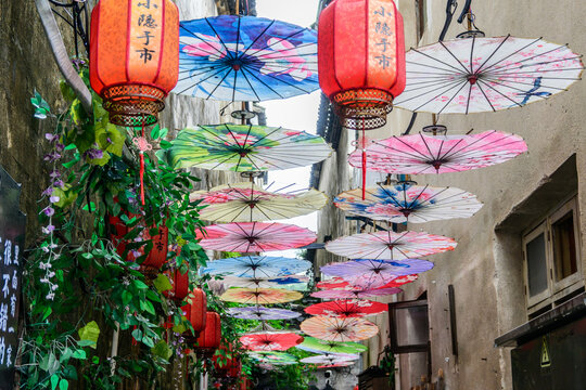 A narrow lane decorated with colorful oiled paper umbrellas and bright red lanterns in Anhui Province near Mount Huangshan, China. These parasols offer shade. - Powered by Adobe