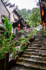 A tranquil scene featuring a stone stairway alongside a waterfall during rain at Huangling Village...
