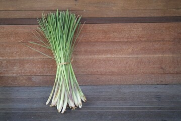 A tied bunch of fresh lemongrass stalks rests on a rustic wooden table, ready for culinary or...