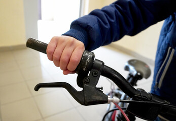 A child is holding onto the handlebars of a bicycle in the entrance. The close-up of the hand on...