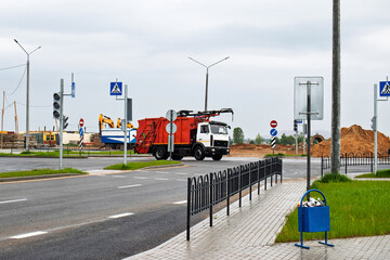 Waste collection truck gathers refuse at busy intersection near construction site on a cloudy day