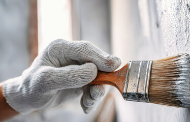 Close-up of gloved hand applying fresh paint to wall at construc