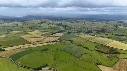 Drone photo of lush green paddocks and fields divided by hedgerows under a cloudy sky.