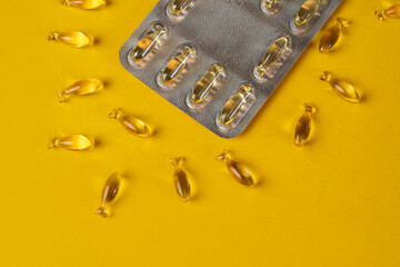 Blister pack with golden yellow Omega-3, Omega-9 capsules in the shape of a fish on a yellow...