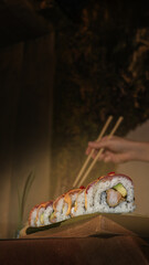 Hand holding sushi roll with chopsticks, showcasing fresh ingredients. Vertical orientation
