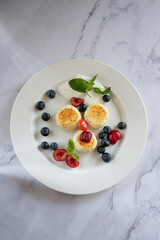 Three delicious cheesecakes with poppy seeds, blueberries, cherries and sour cream on white plate on marble background
