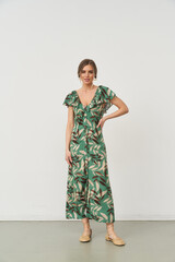 Woman wearing a green dress with a tropical leaf pattern stands confidently on a neutral surface,...