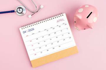 April 2026 desk calendar and stethoscope with piggy bank; Savings for Health insurance concept.