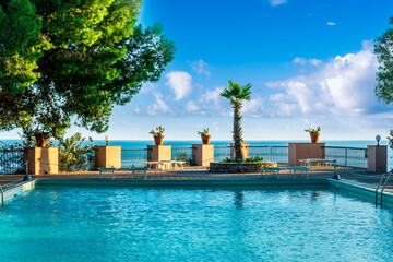 swimming pool with blue water in a hoter resort park during summer tourism season with green trees...