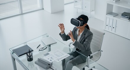 Businesswoman uses VR headset at glass desk in modern office.
