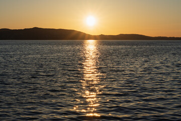 A picturesque evening landscape in Norway. The bright sun over the hills and its golden reflection on the dark water of a Scandinavian fjord.