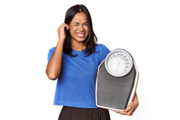Filipino woman with scale in studio covering ears with hands.