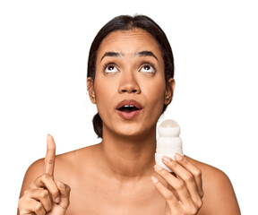 Filipino woman holds deodorant in studio pointing upside with opened mouth.