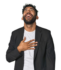 Hispanic businessman in suit in studio laughs out loudly keeping hand on chest.