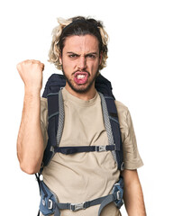 Young Caucasian hiker with backpack showing fist to camera, aggressive facial expression.