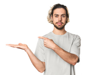 Young Caucasian man in studio setting excited holding a copy space on palm.