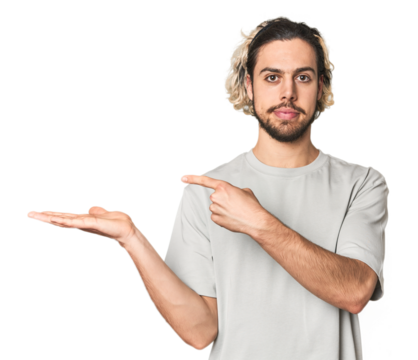 Young Caucasian man in studio setting excited holding a copy space on palm.