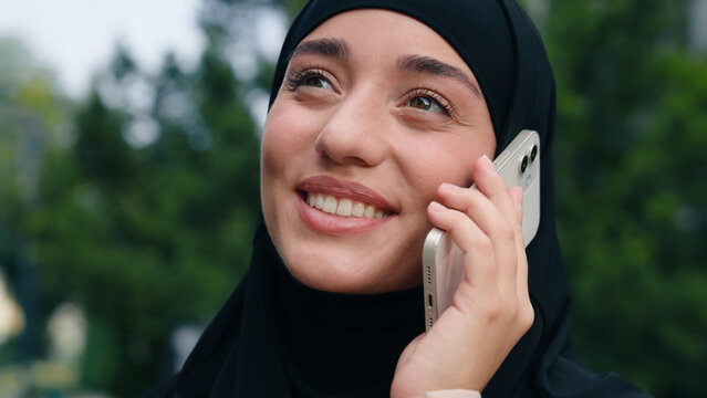 Portrait happy smiling Muslim business woman Islamic businesswoman girl female in black hijab employer in city positive communicate talking mobile phone smartphone friendly conversation talk outdoors