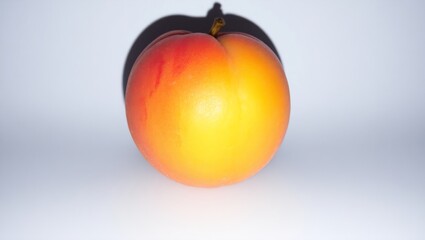 High-res close-up of a ripe peach against a white background. Vibrant red, orange, and yellow hues with subtle fuzz and soft shadow, highlighting its natural beauty.









