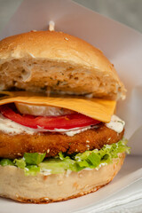 A delicious hamburger showcases layers of flavorful beef patties, melted cheese, crisp lettuce, tomato and cucumber, and sesame seed bun, served on a white plate.