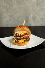 A delicious hamburger showcases layers of flavorful beef patties, melted cheese, crisp lettuce, tomato and cucumber, and sesame seed bun, served on a white plate.