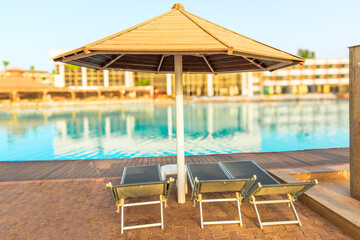 Sun loungers and umbrella by the pool with clear azure water in the tropics