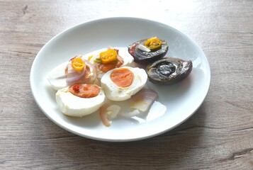 boiled salty and black preserved egg half cut with slice shallot and chili salad on plate