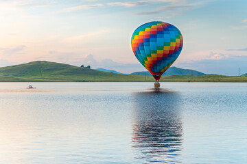 Colorful hot air balloon flying over the lake at sunset. Beautiful summer landscape.