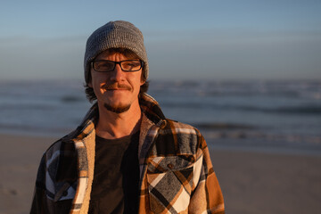 Happy Man in Plaid warm Shirt, Beanie and Glasses by the Ocean