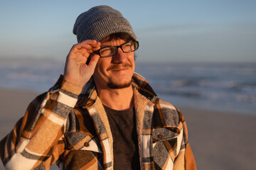 Happy Man in Plaid warm Shirt, Beanie and Glasses by the Ocean