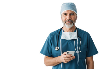 Confident senior male doctor wearing scrubs, cap, and stethoscope, holding a smartphone, symbolizing modern healthcare communication and professionalism
