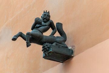 A quirky bronze statue of a crowned centaur king holding a beer mug on a historic building wall