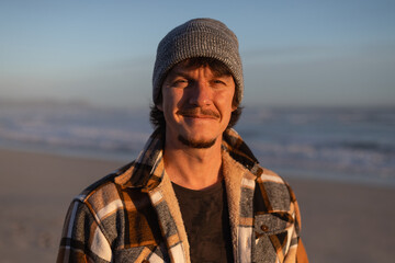 Happy Man in Warm Plaid Shirt and Beanie by the Ocean