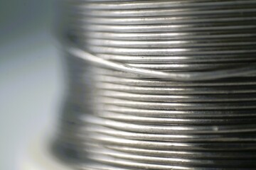 Close-up of a spool of shiny metallic wire, showcasing its texture and parallel lines. Ideal for...