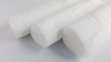 Close-up shot of three rolled gauze bandages on a white background.  Clean, sterile, medical supplies.