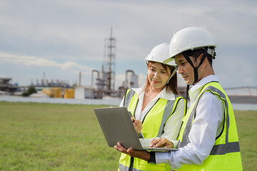 Engineers with Laptop Analyzing Data at Construction Site. Two people wearing safety vests and hard hats looking at a laptop