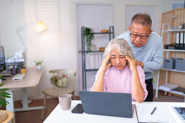 Stressed Older Asian Woman Working From Home with Supportive Husband Massaging Her Head Senior Couple Managing Finances Online on Laptop